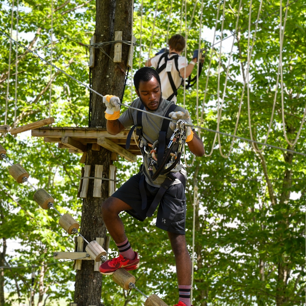 guy climbing in treetop ropes course 